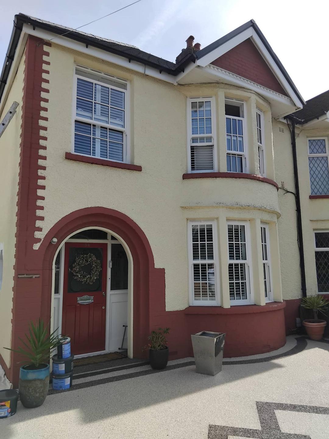 Semi-detached house before repainting, cream render with worn dark red masonry detailing